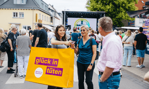 Frau mit einer riesigen bedruckten Tüte spricht mit Passanten.